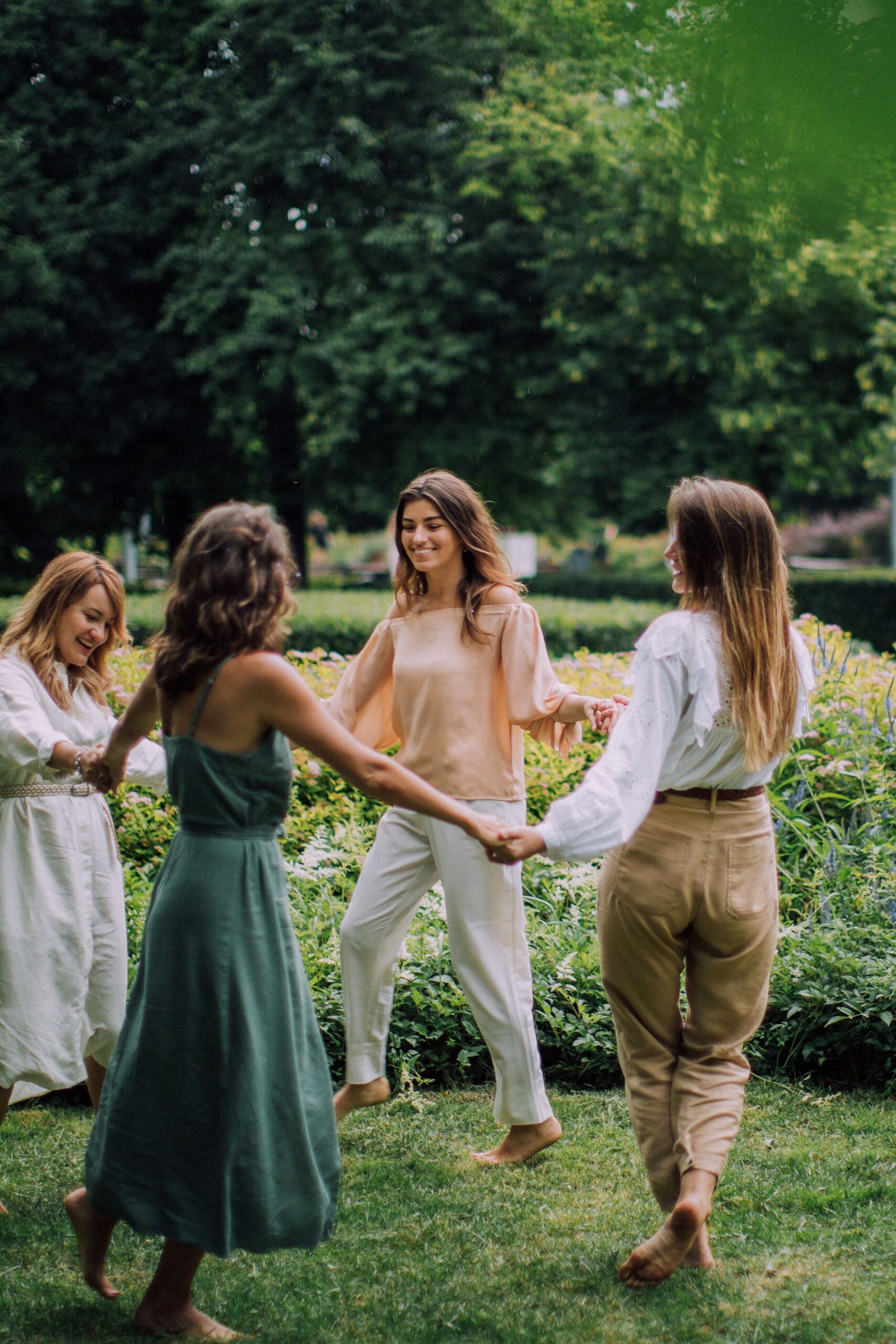 Four women dancing barefoot in a park, celebrating friendship with a joyful picnic.
